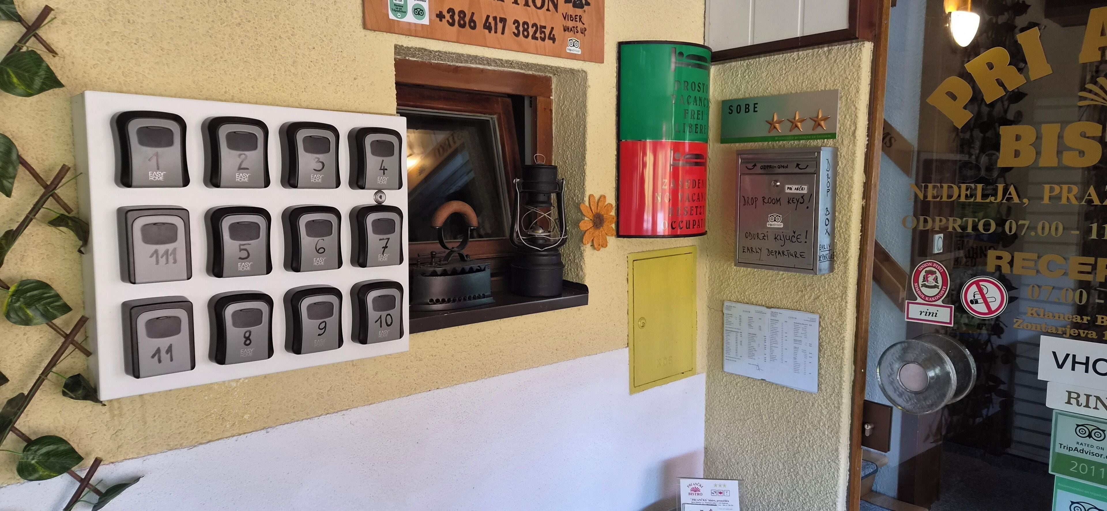 A wall with numbered room keys, a drop room key, and various signs including a rating and a TripAdvisor logo.