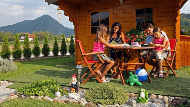 Una cabaña de madera con una mesa y sillas para comer, rodeada de un jardín cuidado y una montaña al fondo.