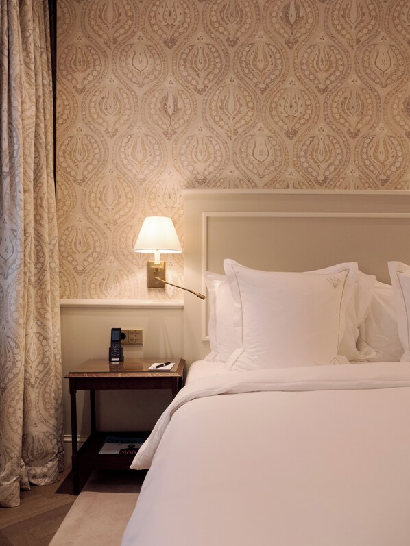 A hotel room with a bed, a nightstand with a lamp, and a patterned wallpaper.