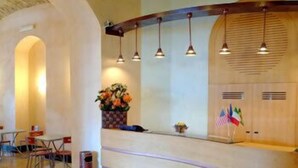Un área de recepción con un mostrador de madera, varias lámparas colgantes y una planta en maceta.