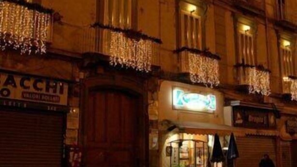 Un edificio con varias ventanas, algunas con luces colgantes. Se ven letreros de un restaurante y una tienda.