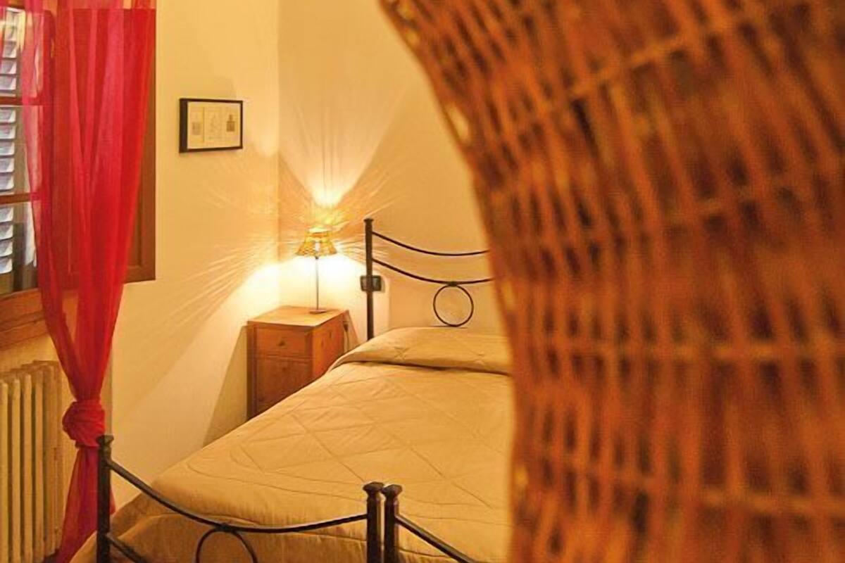 A bedroom with a bed, a nightstand, a lamp, and a red curtain.