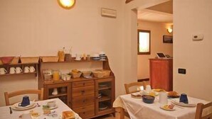 A dining area with wooden cabinets, a table set for two, and a shelf with kitchen items. - Arco Antico (Florence)