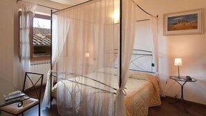 A room with a bed under a mosquito net, a small table with a lamp, and a painting on the wall. - Arco Antico (Florence)