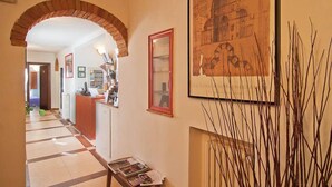 A hallway with a tiled floor, a reception desk, framed artwork, and a brick archway. - Arco Antico (Florence)