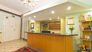 A reception area with a counter, a chandelier, a bookshelf with magazines, and a door with a sign. - Hotel Pension Stadtpark (Vienna)