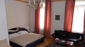 A bedroom with a bed, a black sofa, a coffee table, and a chandelier. - Hotel Pension Stadtpark (Vienna)