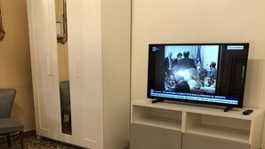 A room with a television on a stand, a grey sofa, a white wardrobe, and a grey carpet. - B&B Accorsi (Bologna)
