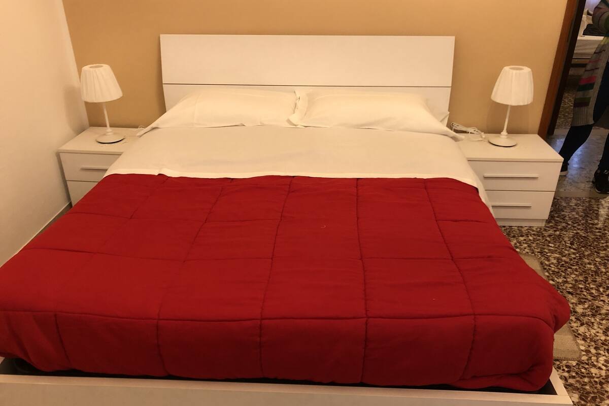 A bed with a white headboard, two bedside tables with lamps, and a red bedspread.