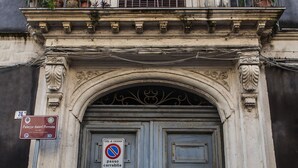 Un bâtiment historique doté d’une grande porte à double battant richement décorée et d’un balcon agrémenté de plantes en pot.