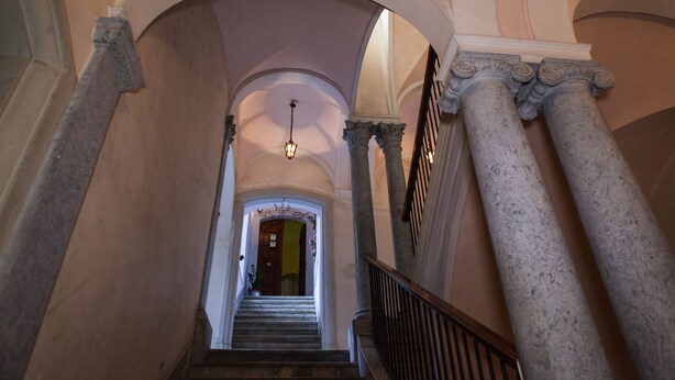 Un magnifique escalier à l’architecture classique, orné de colonnes et d’arcades, mène à une porte située au bout.