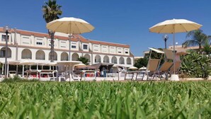 Un hôtel doté d’une cour intérieure aménagée avec des espaces de détente en plein air et des parasols, le tout entouré de palmiers et d’une pelouse bien entretenue.