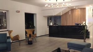 Un espace d’accueil moderne avec un comptoir noir, des chaises bleues et jaunes, et une grande horloge murale.