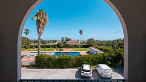 Une vue à travers une fenêtre en arc d’un quartier résidentiel, avec une piscine, des voitures garées et des palmiers.