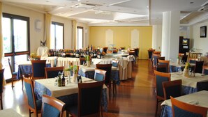 Un espace repas comprenant plusieurs tables et chaises, une variété de bouteilles de vin exposées et une grande fenêtre laissant entrer la lumière naturelle.
