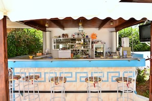 A bar area with a blue counter, metal chairs, and various bottles and glasses. - Sun City (Chania)