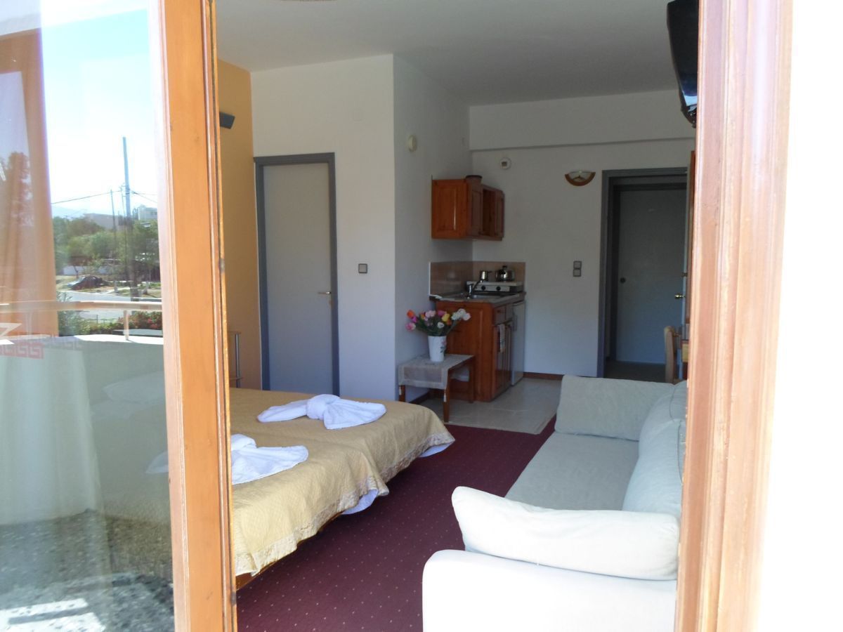 Ein Zimmer mit einem Bett, einer Sitzecke, einer Küchenzeile und einer Tür zum Balkon.