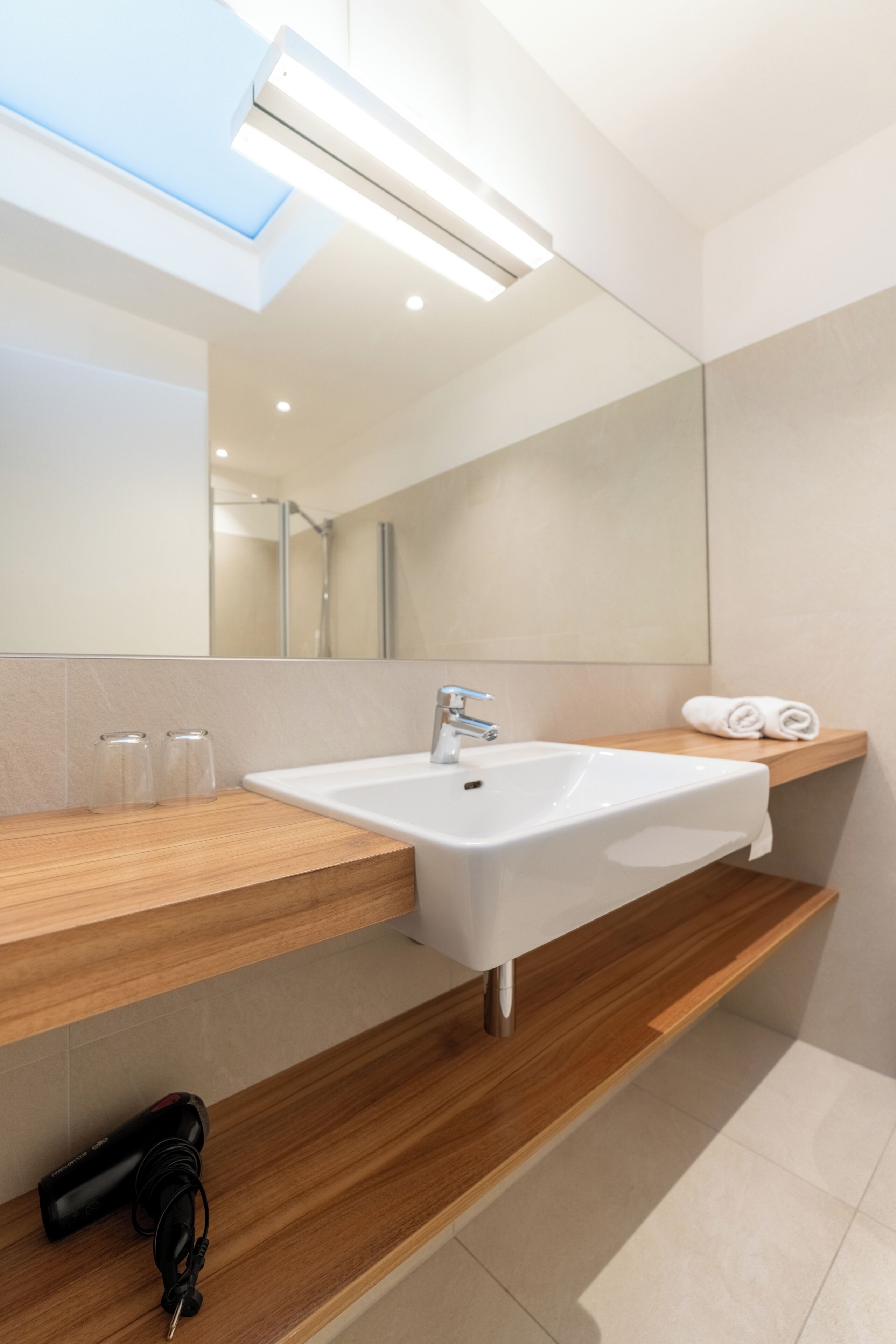 A modern bathroom with a large mirror, a white sink, and a towel rack.