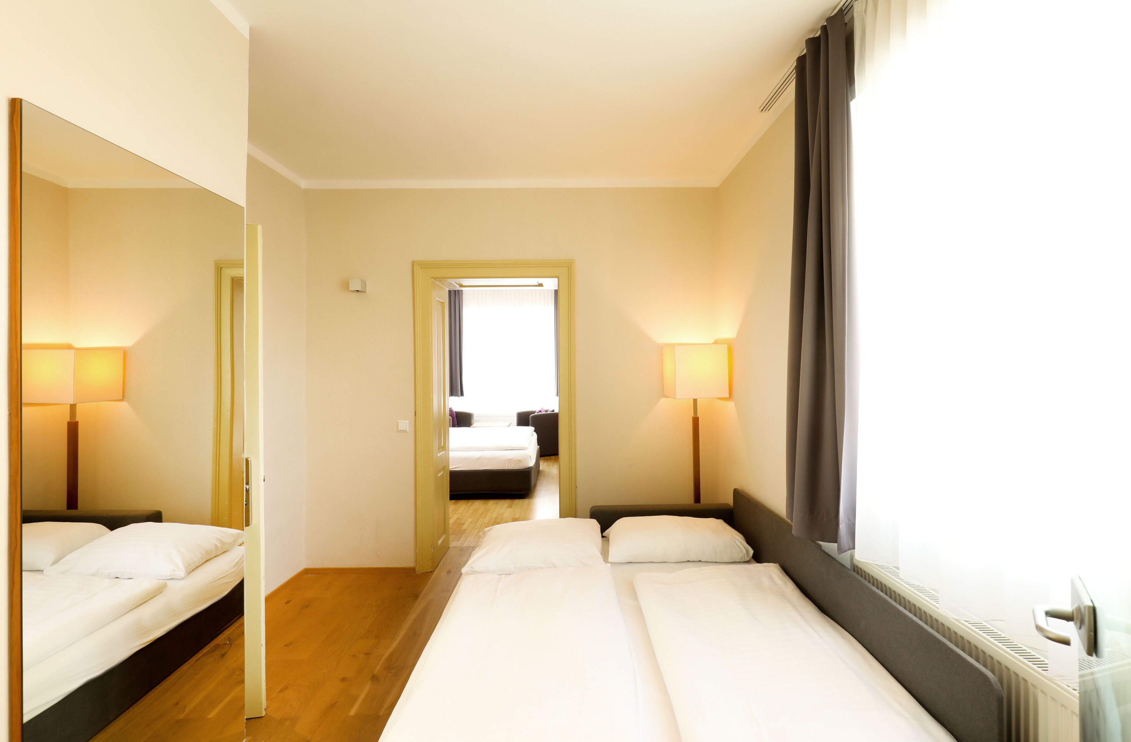 A hotel room with two beds, a large mirror, and two bedside lamps.