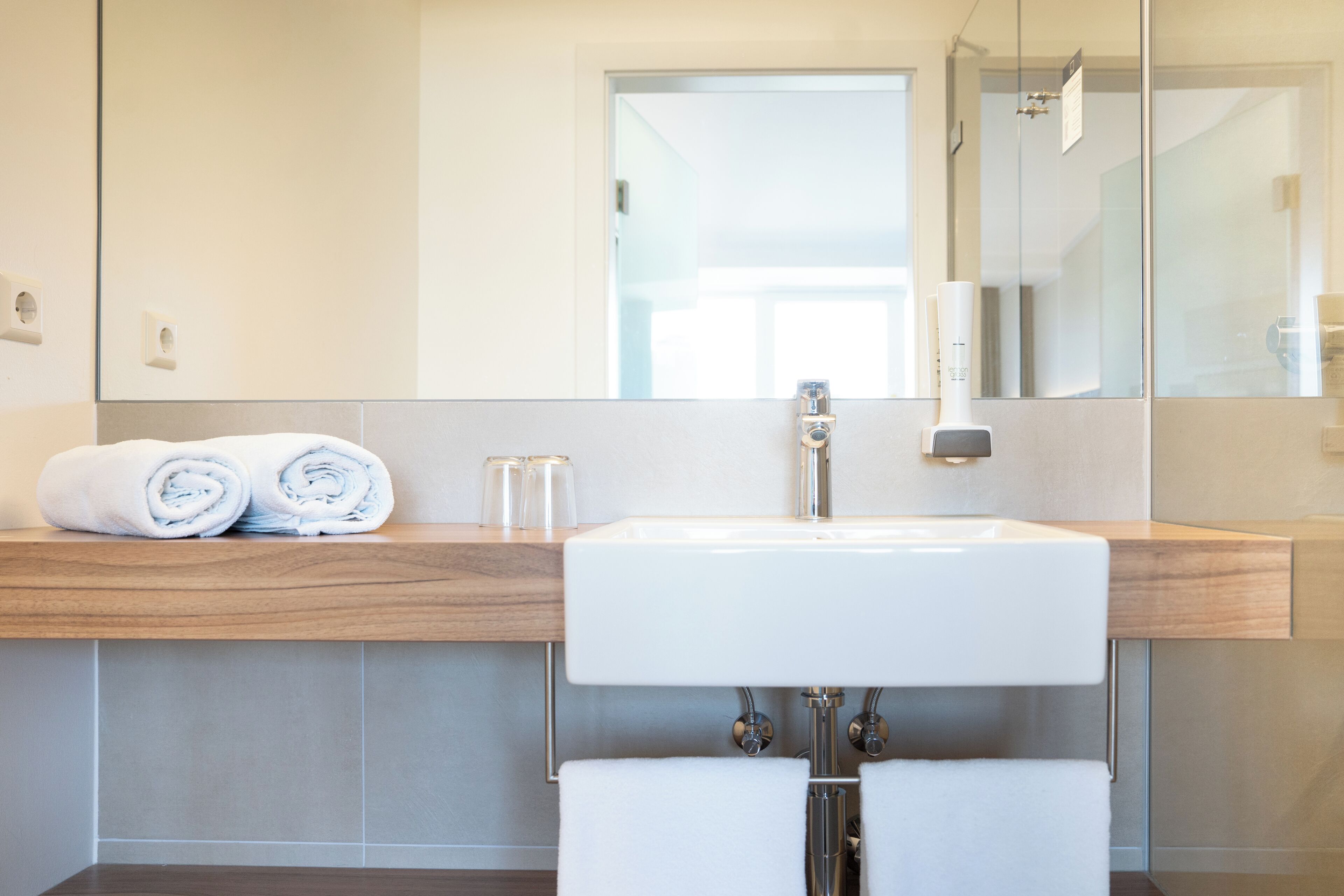 Een moderne badkamer met een grote spiegel, een witte wastafel en netjes opgevouwen handdoeken op een houten aanrecht.