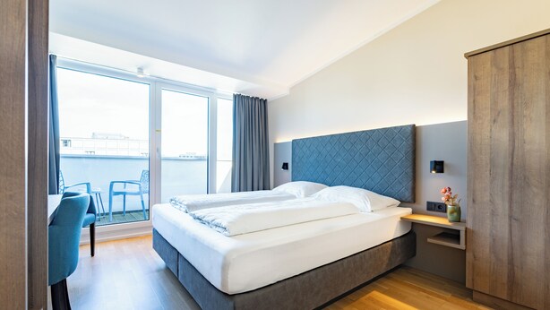 A modern hotel room with a large bed, a desk, and a view of the water. - Das Jedermann Boutiquehotel (Salzburg)