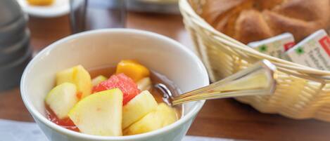 A bowl of fruit salad with a spoon, a basket of bread, and a cup of coffee on a table.