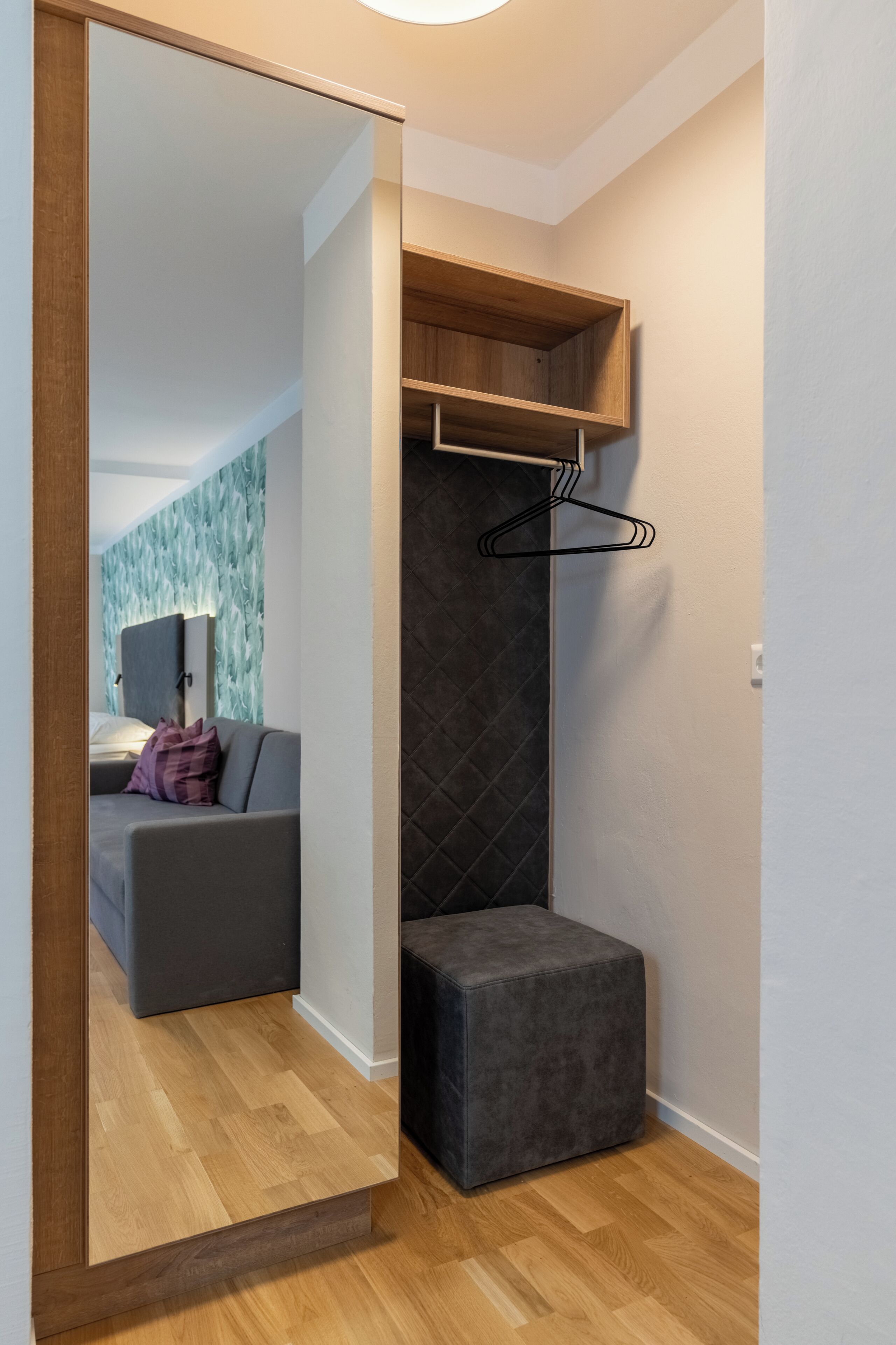 Una habitación moderna con piso de madera, un sofá gris, un reposapiés negro, un estante de madera y un perchero en la pared.