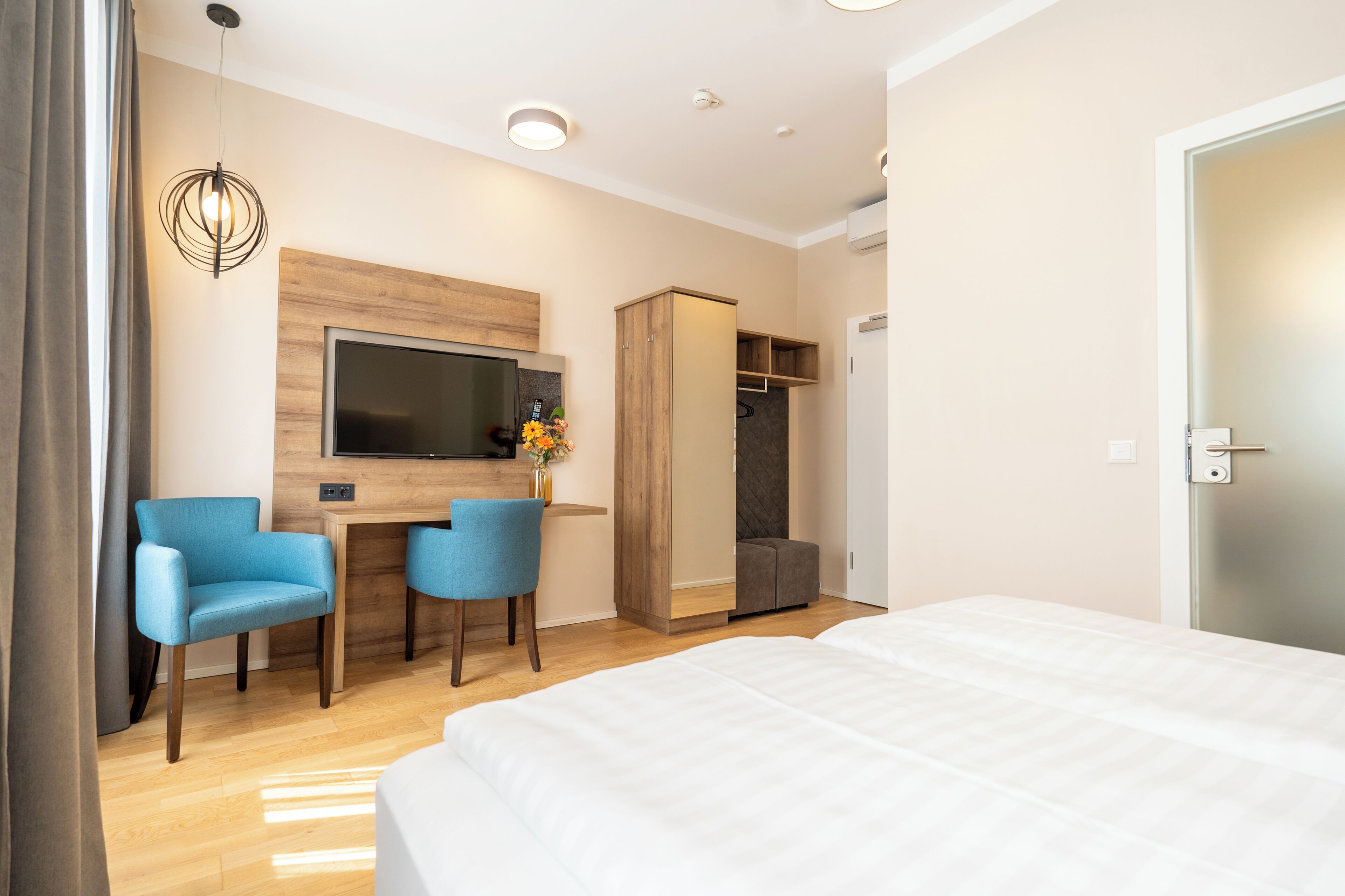 A hotel room with a bed, a desk with two chairs, a television, and a wardrobe.