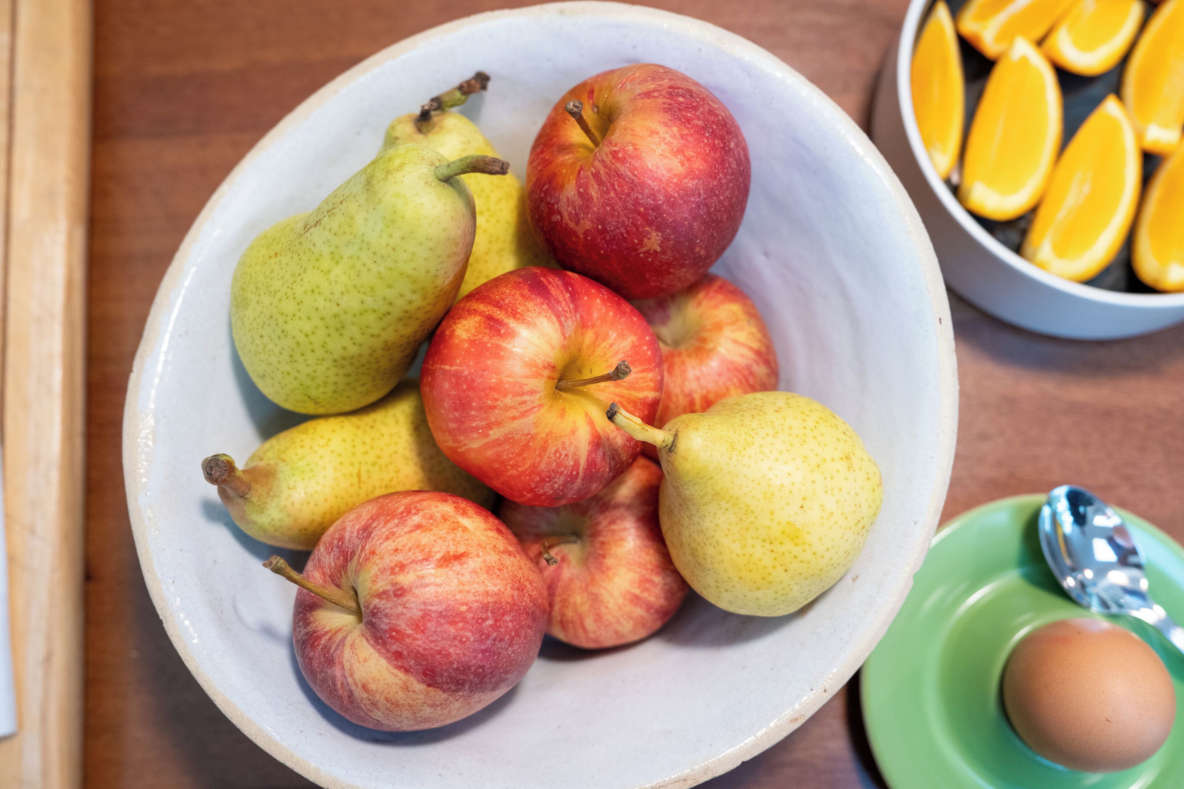 Un bol de frutas, incluyendo peras y manzanas, un bol de rodajas de naranja y una cuchara sobre un plato verde.