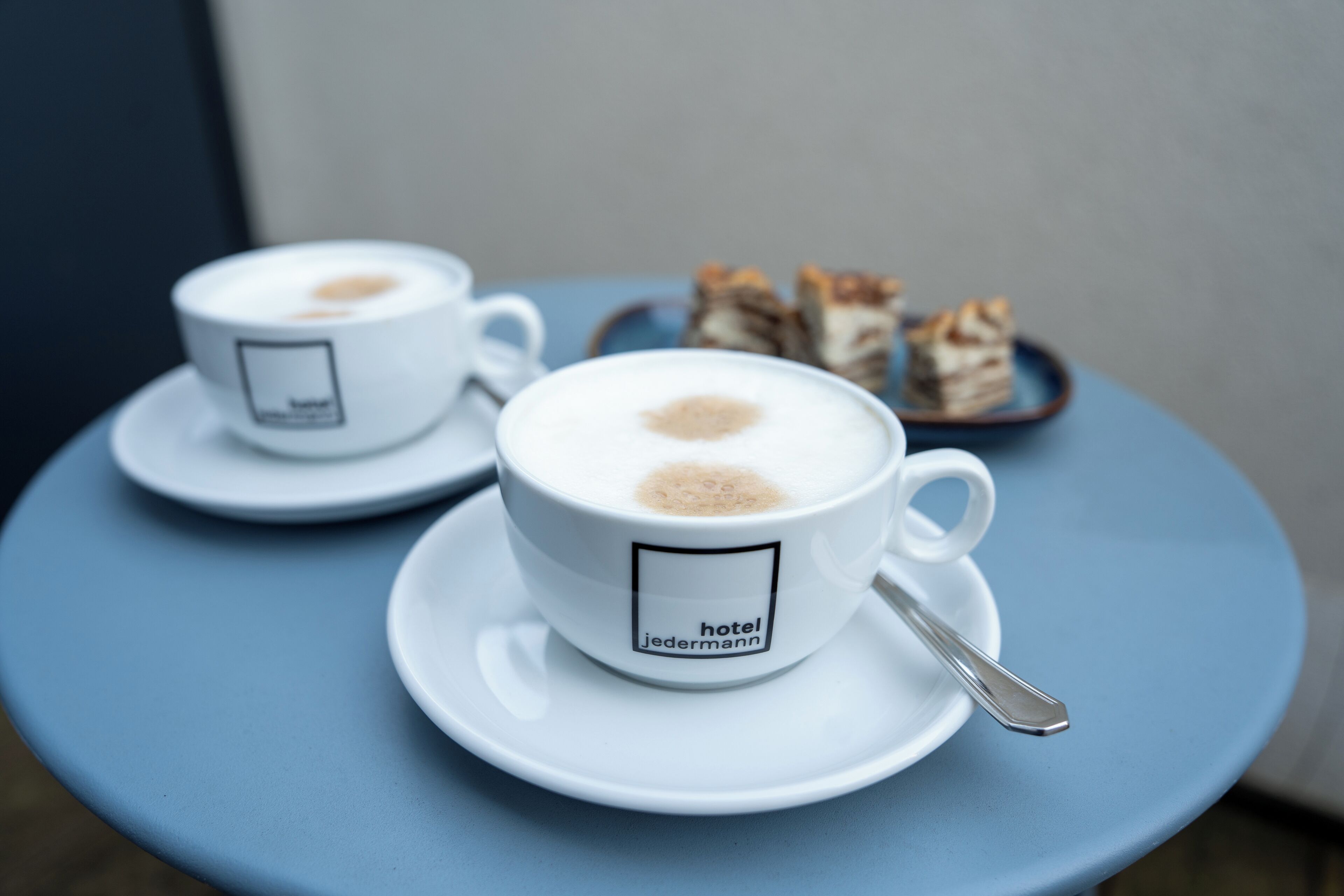 Two white cups of coffee on a blue table with a spoon.