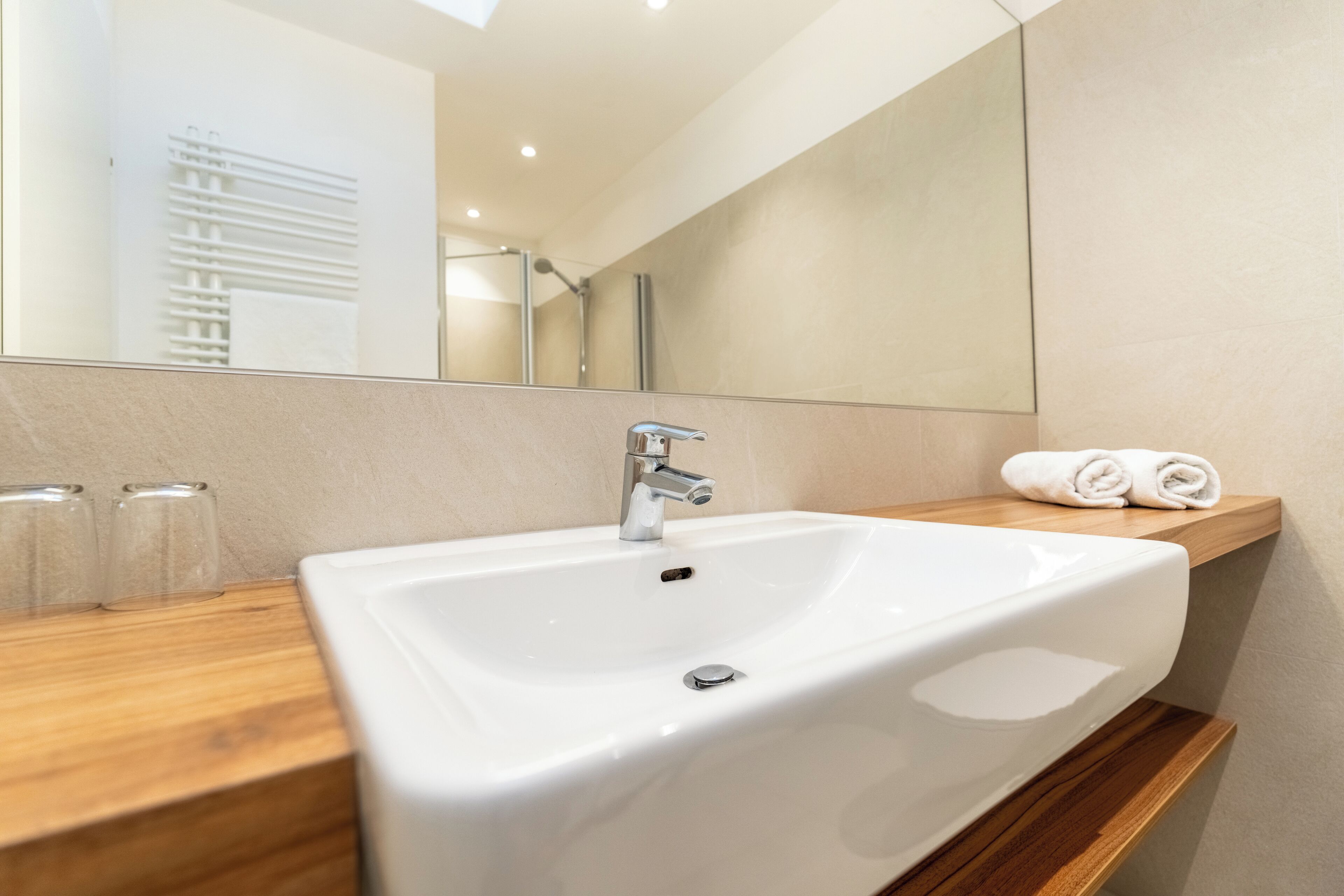 Un baño moderno con un lavabo blanco, un espejo y un estante de madera con toallas.