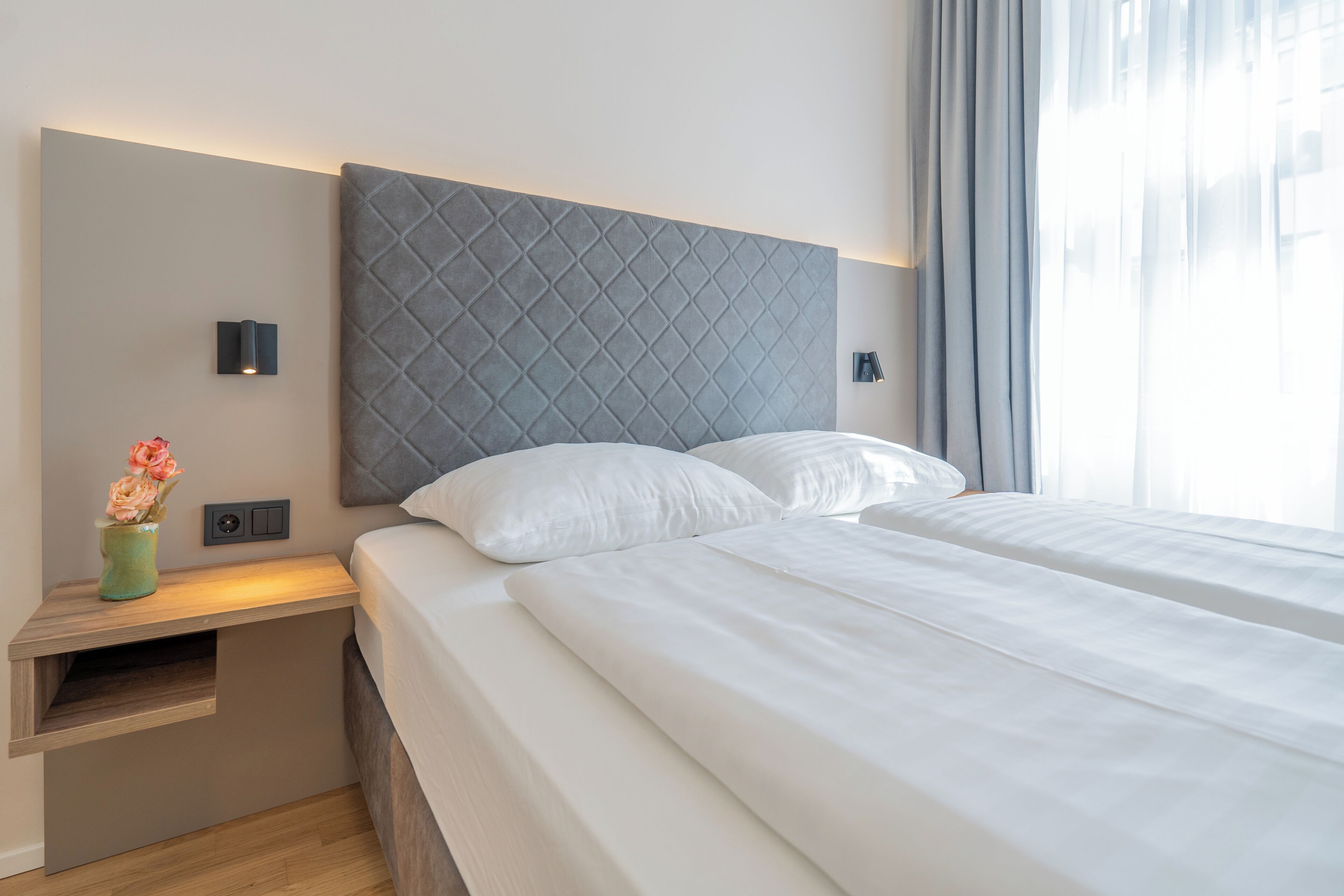 A neatly made bed with a padded headboard, bedside tables with lamps, and a vase with flowers.