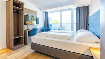 A hotel room with a bed, a desk, a chair, a wardrobe, and a large window.