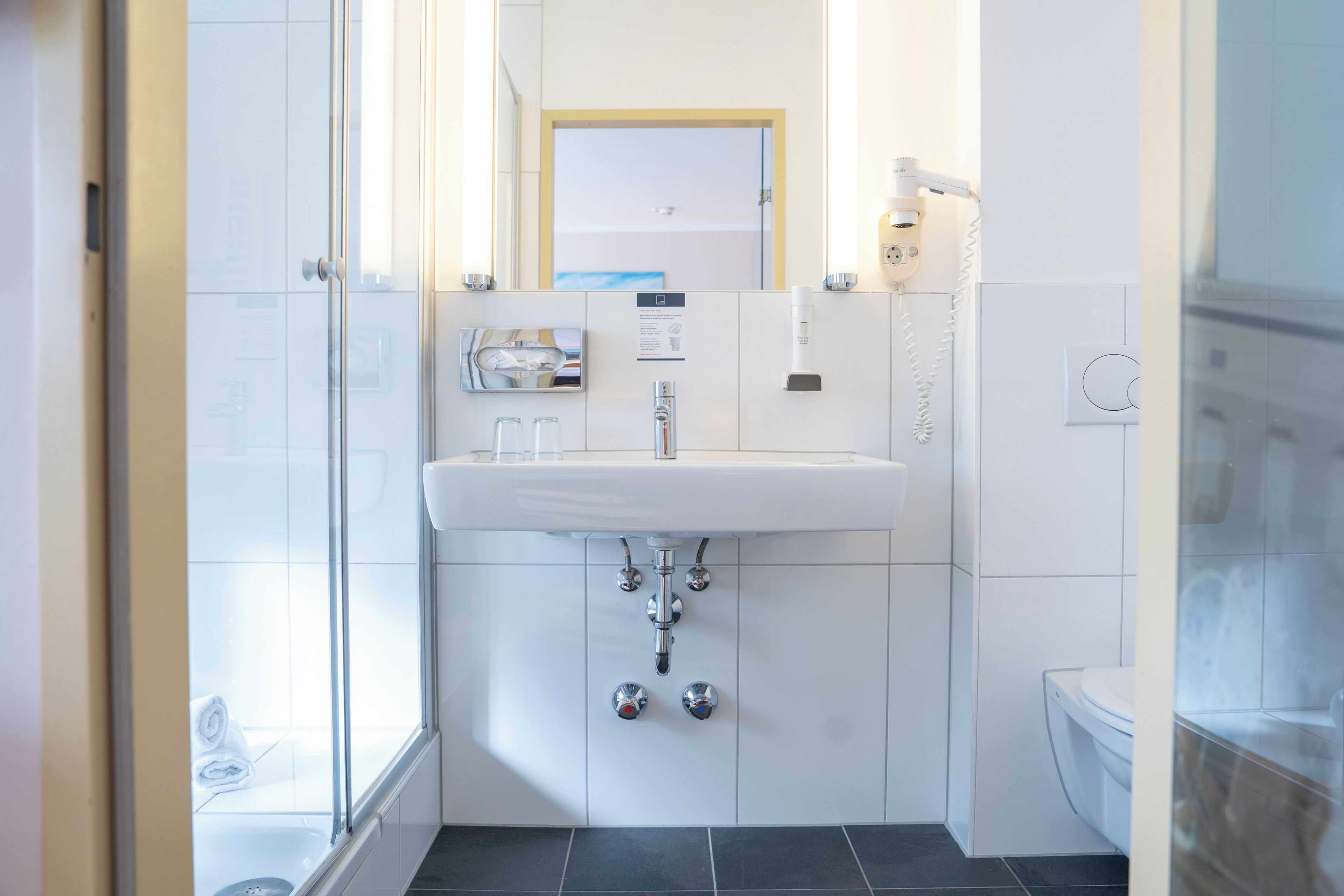 Un baño moderno con un lavabo blanco, un espejo y un inodoro.