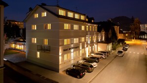 A multi-story hotel with a row of parked cars in front. - Das Jedermann Boutiquehotel (Salzburg)