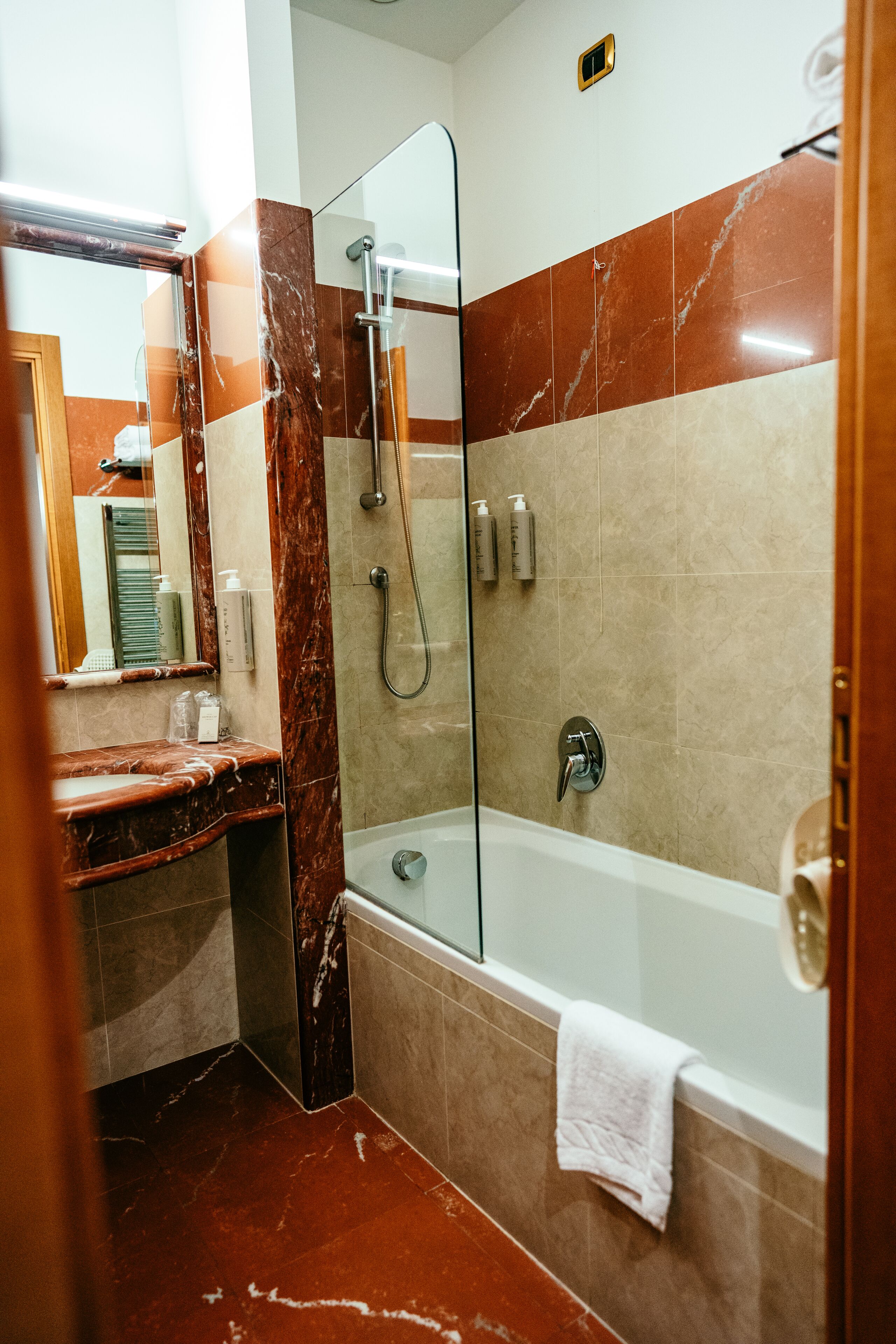 A modern bathroom with a glass-enclosed shower, a marble-tiled wall, and a white bathtub.