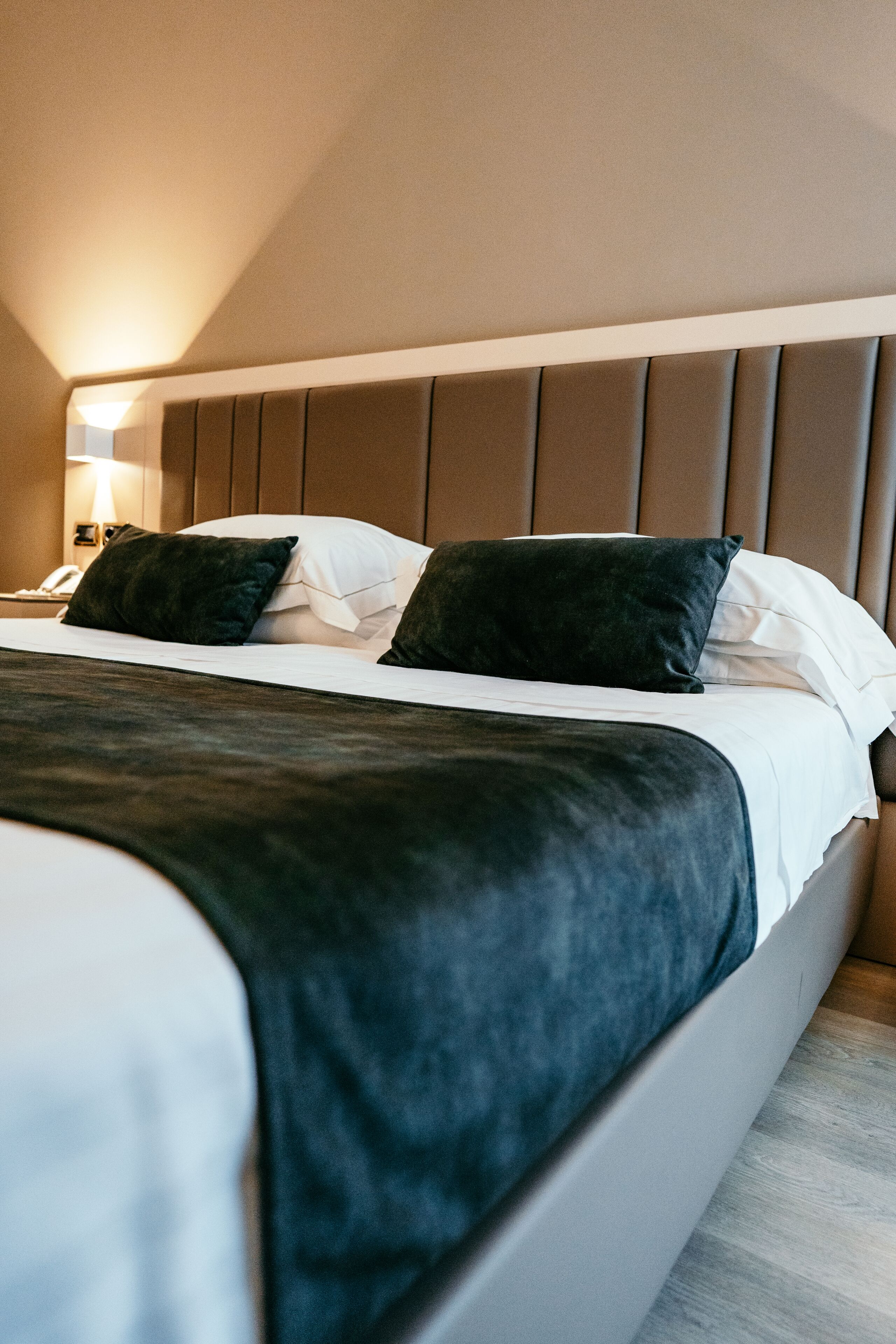 A neatly made bed with a dark headboard, white linens, and two dark pillows.