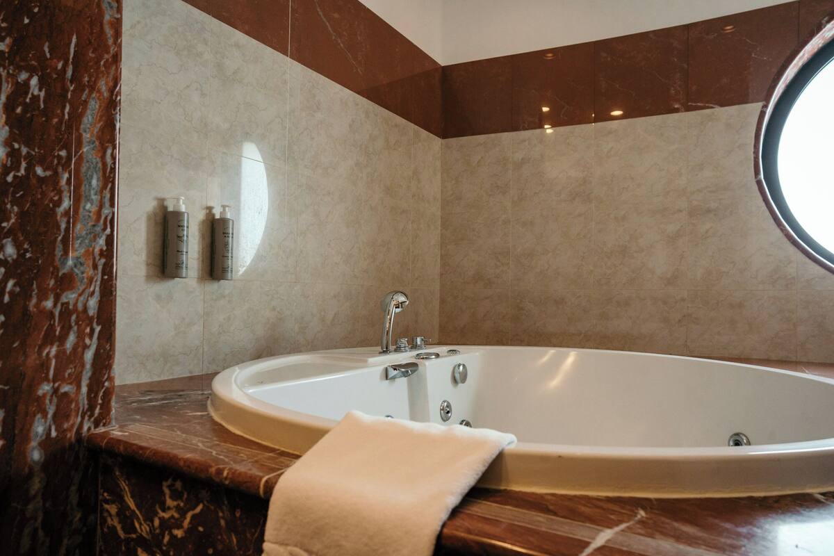 A modern bathroom with a freestanding bathtub, marble walls, and a round mirror.