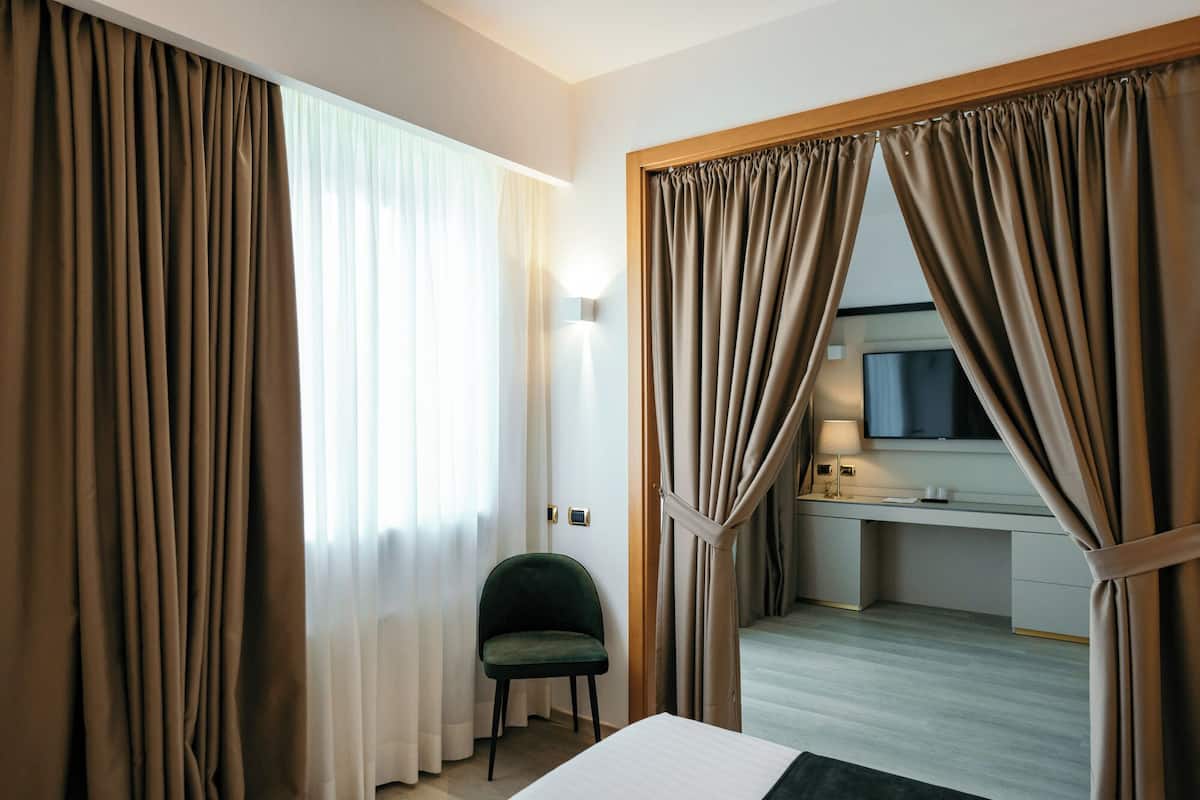 A hotel room with a bed, a chair, a desk with a TV, and curtains.
