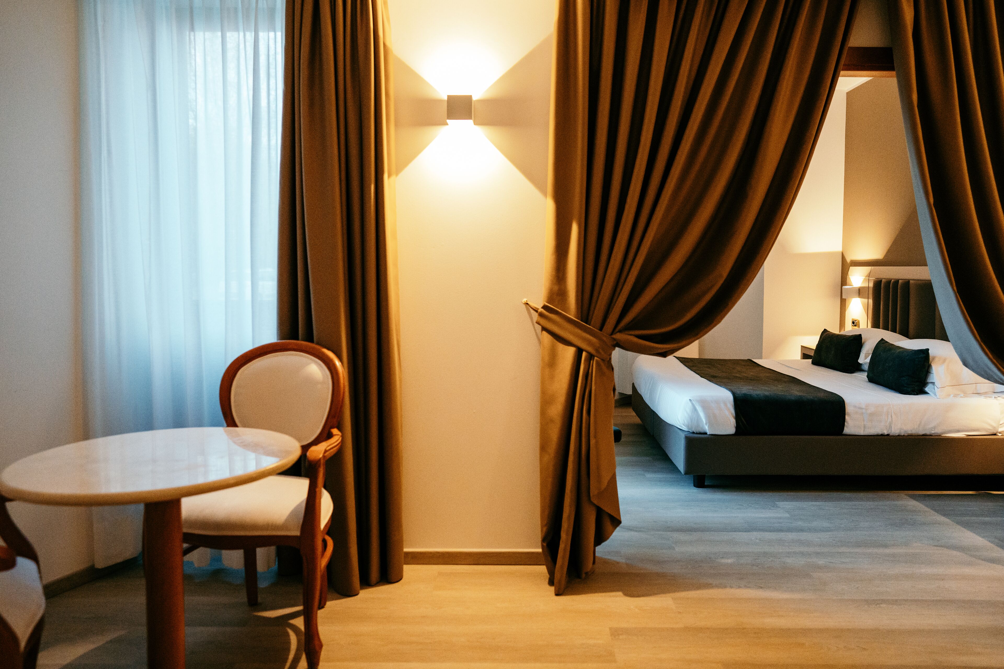 A hotel room with a bed, a chair, a table, and curtains.