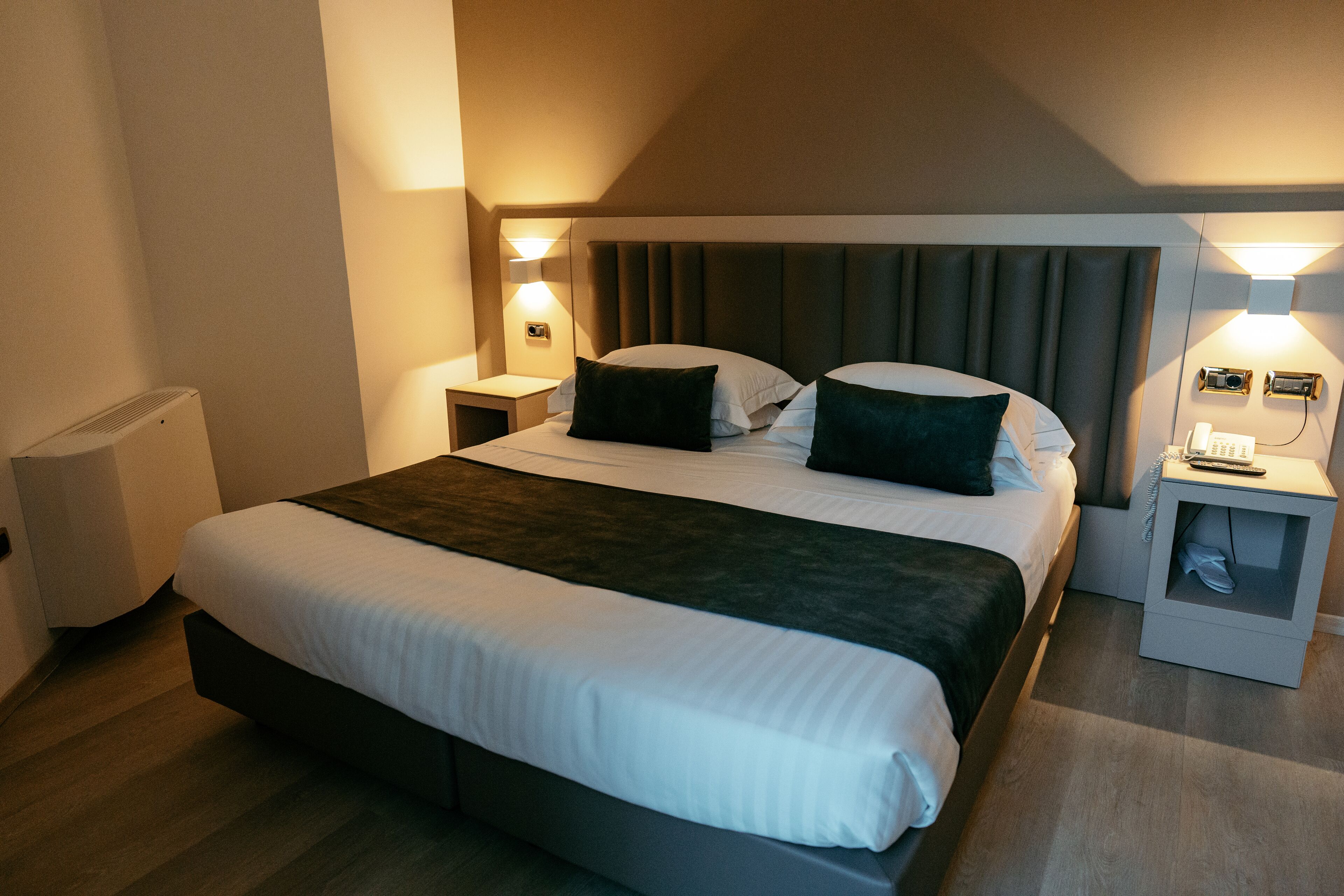 A hotel room with a large bed, two bedside tables, a headboard, and a wall-mounted phone.