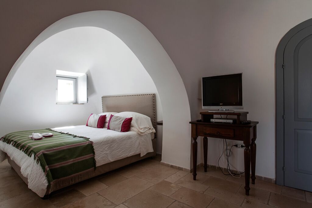 Une chambre à coucher avec un lit, un téléviseur posé sur un meuble en bois et une porte.