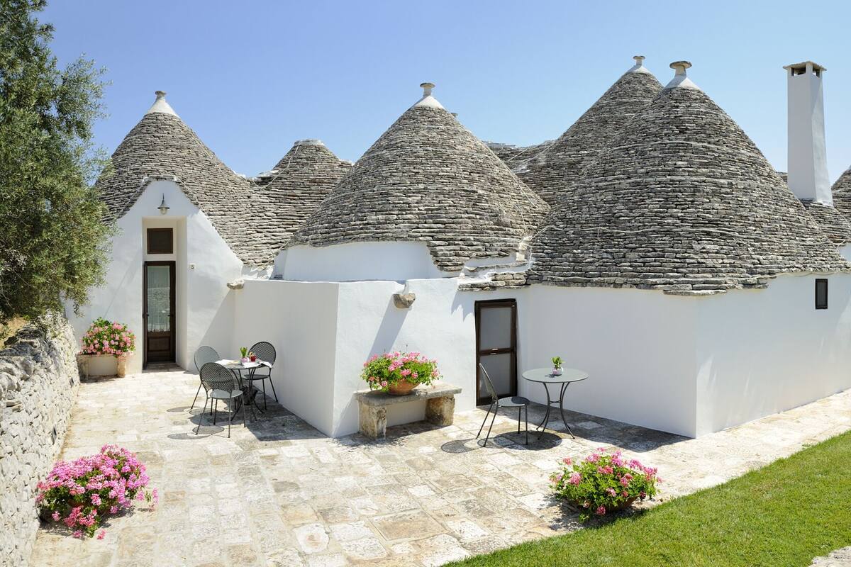 Un bâtiment traditionnel avec un toit en pierre, doté d’un patio, de sièges en plein air et de plantes en pot.