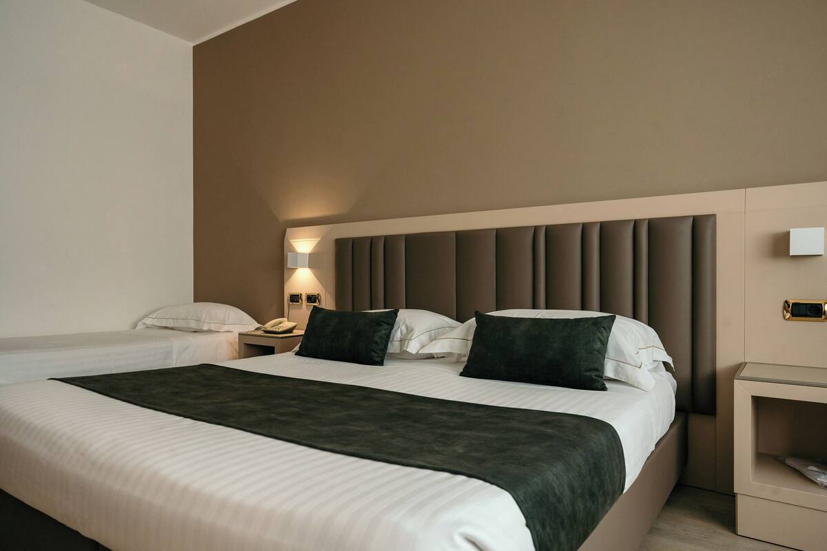 A hotel room with a large bed, two bedside tables, a wall-mounted phone, and a bedside lamp.