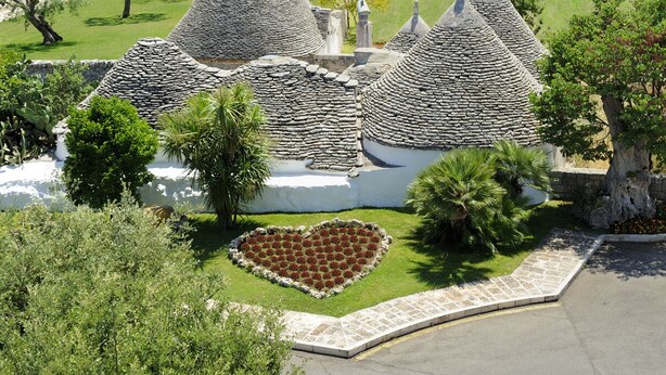 A series of stone-roofed buildings with a heart-shaped flower bed in the foreground. - Grand Hotel La Chiusa di Chietri (Alberobello)