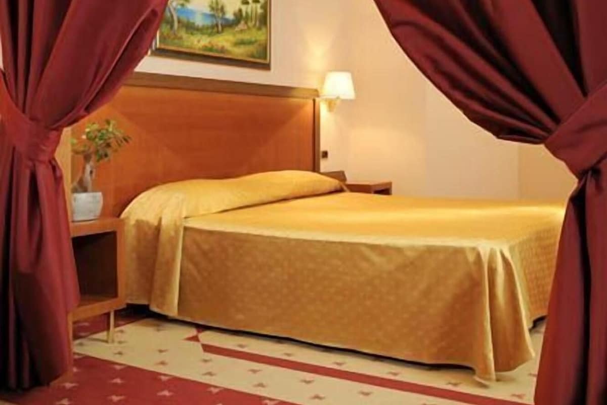 Una habitación de hotel con una cama, una mesita de noche, una lámpara y un cuadro en la pared.