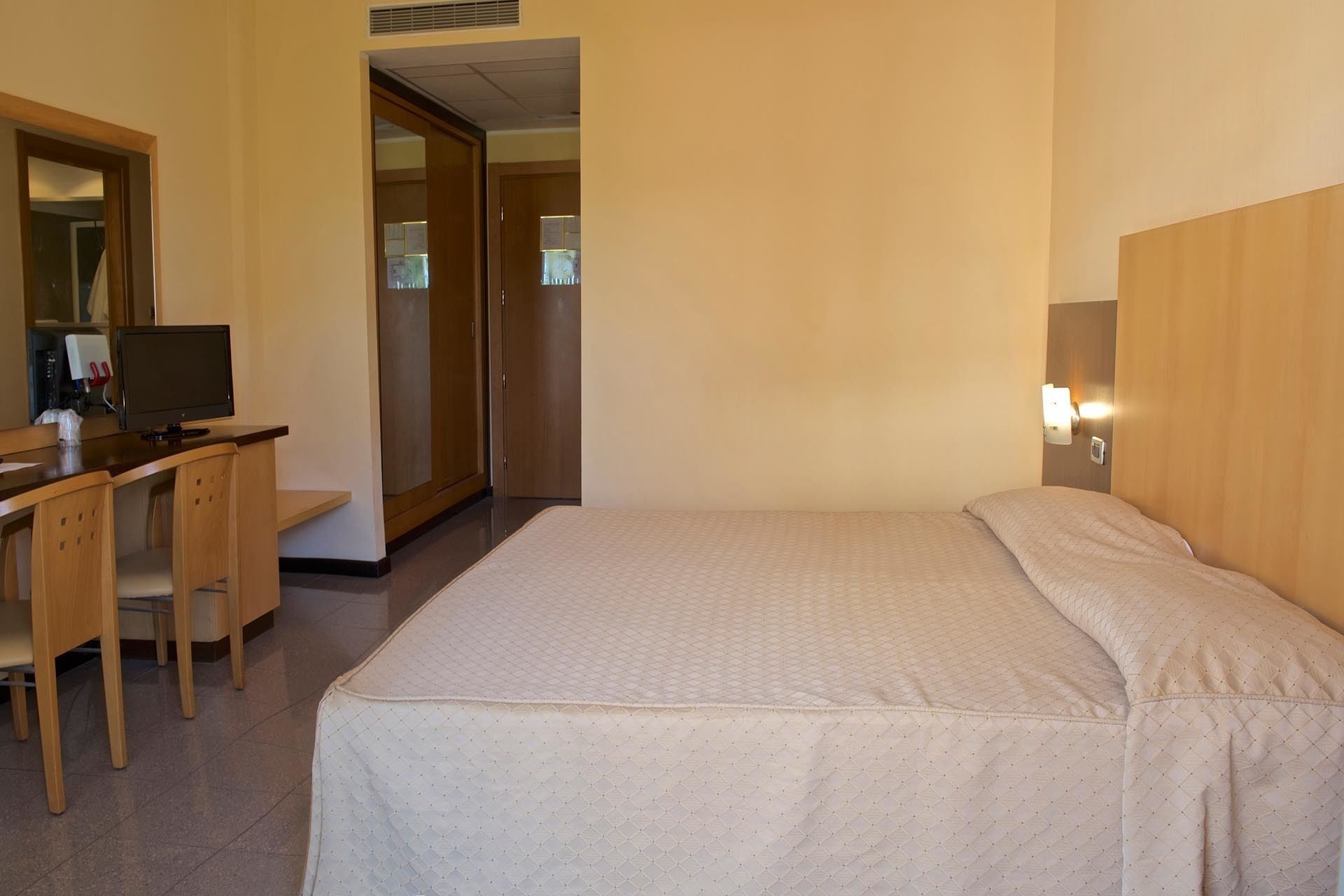 Une chambre d’hôtel comprenant un lit, un bureau avec un ordinateur, un miroir et une armoire.