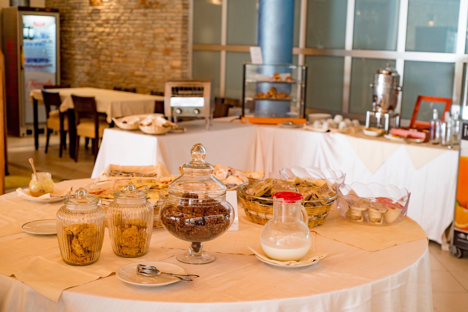 A buffet table with various food items and condiments, including jars of preserves and a pitcher of milk.