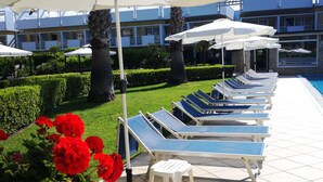 A poolside area with lounge chairs and umbrellas, a well-maintained lawn, and a building in the background.