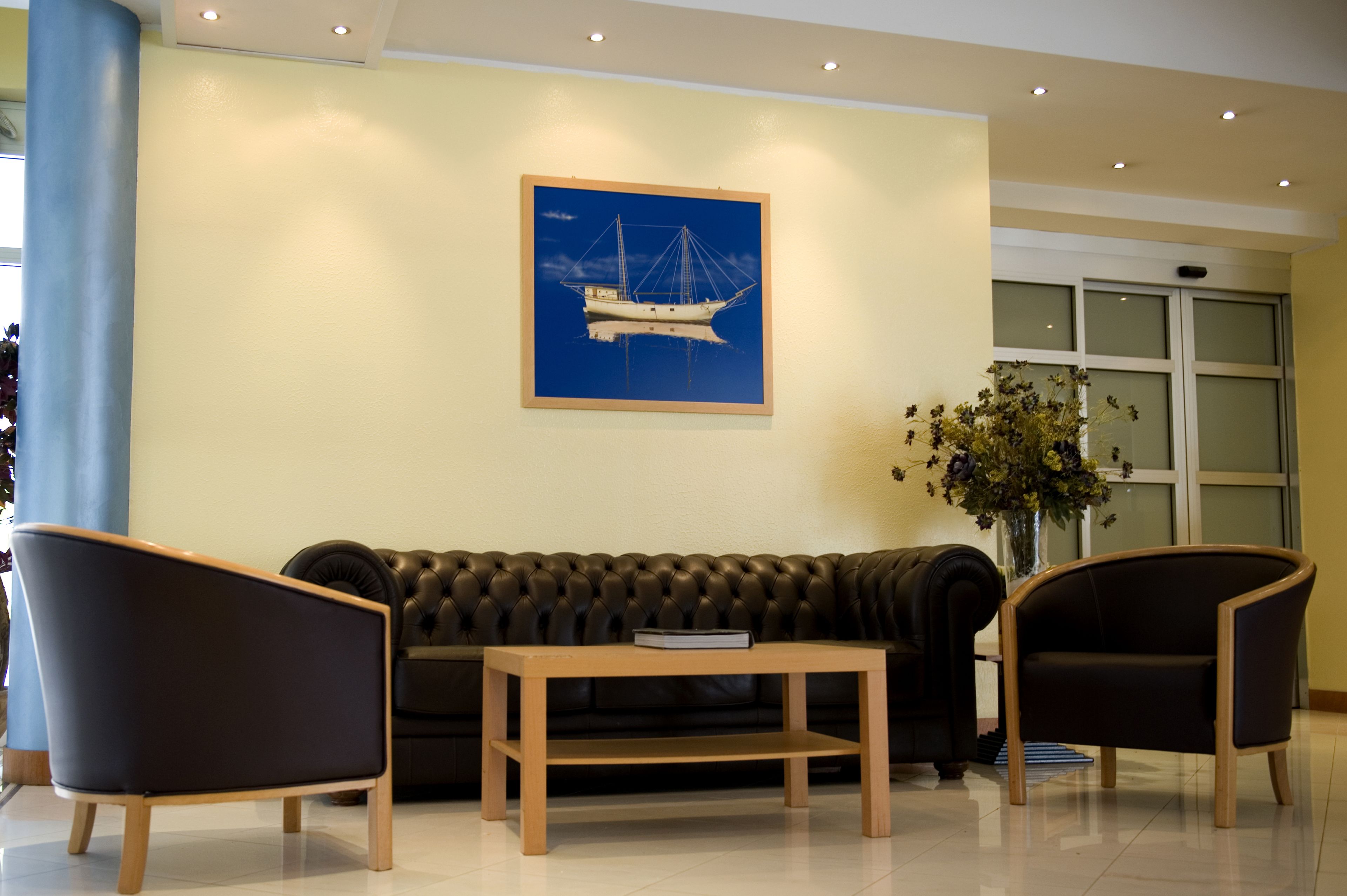 Un vestíbulo moderno con un sofá de cuero oscuro, dos sillones, una mesa de centro de madera y un cuadro enmarcado con motivos náuticos en la pared.